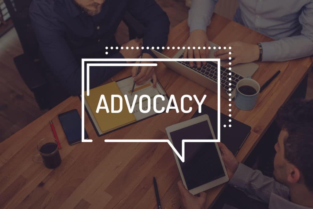 ‘Advocacy’ in a speech bubble overlaid on a photo of people sitting at a table.
