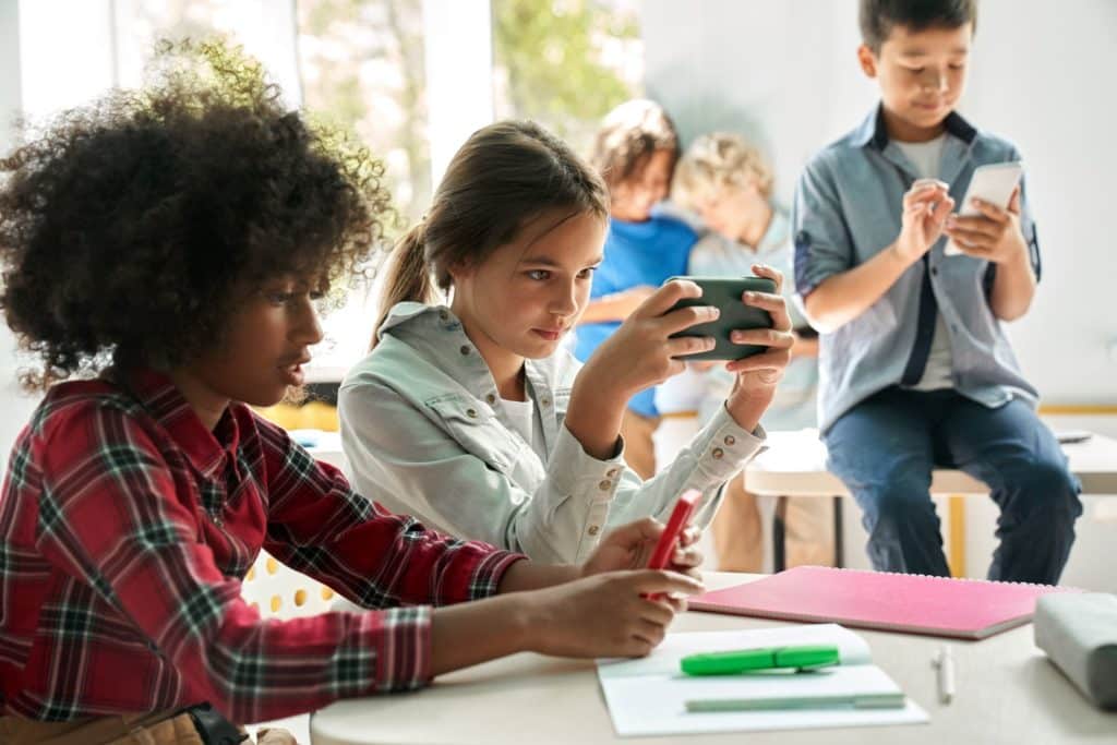 Students sit at their desk, all using their smartphones.