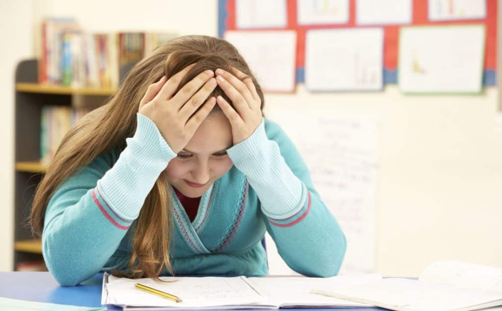 Female student with elbows on desk holding head in her hands