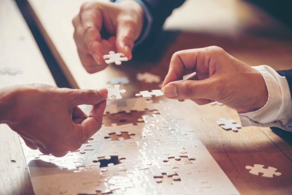 Three hands hold a piece of a puzzle, representing the stakeholders in education who come together to make the entire picture.