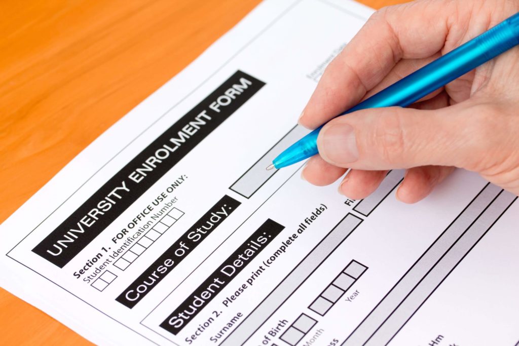 Hand holding a pen completes a university application form.