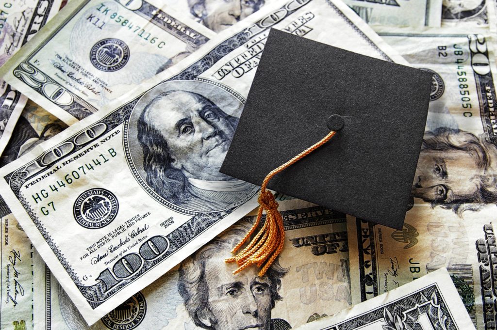 Graduation cap on top of a pile of hundred dollar bills.