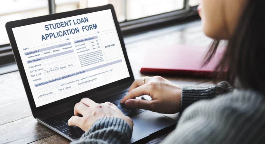 A student sits at their laptop, filling out a student loan application.