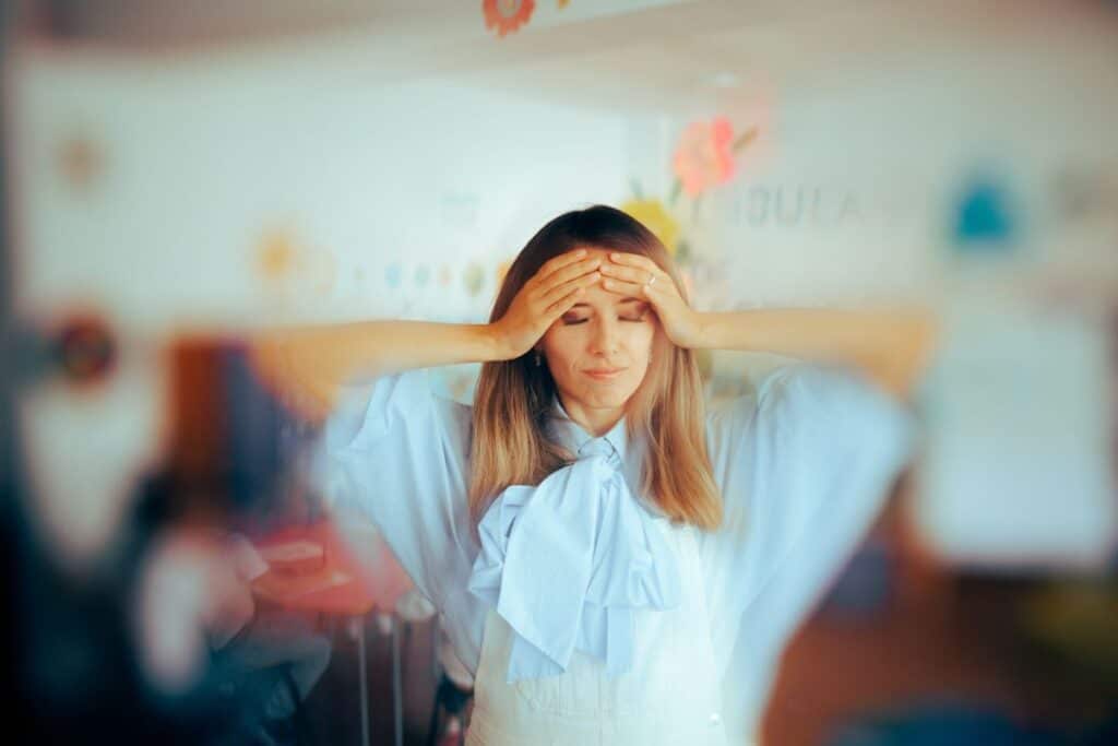 A teacher holds her head, appearing very anxious and stressed.