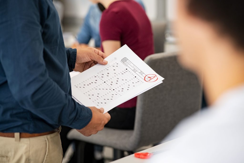 Close up of a teacher handing back tests with the grade “A” circled on top of one.