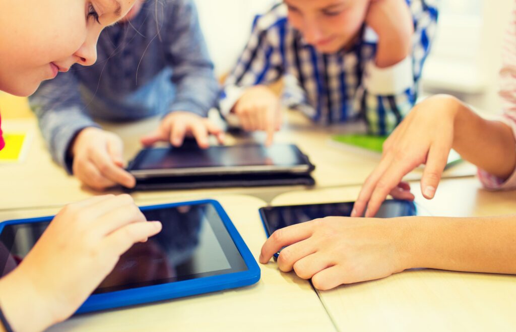 A group of elementary age students use their tablets and phones in the classroom.