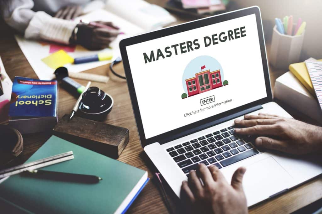 Someone sitting at a table using their laptop and looking at master’s degree