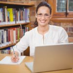 A teacher works on a laptop in the library.