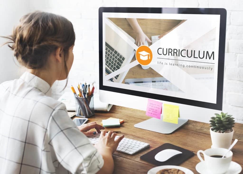 Young woman sitting at a desk using a computer with ‘Curriculum’ on the screen.